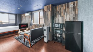 Una camera moderna con soffitto in legno, televisione a schermo piatto, angolo cottura e una grande finestra.