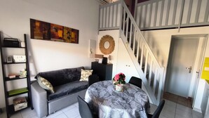 Een woonkamer met een bank, een tafel met een patroon tafelkleed, een trap en een deur.
