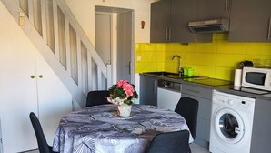 Een compacte keuken met een wasmachine, een eettafel met stoelen en een trap naar een hoger gelegen verdieping.