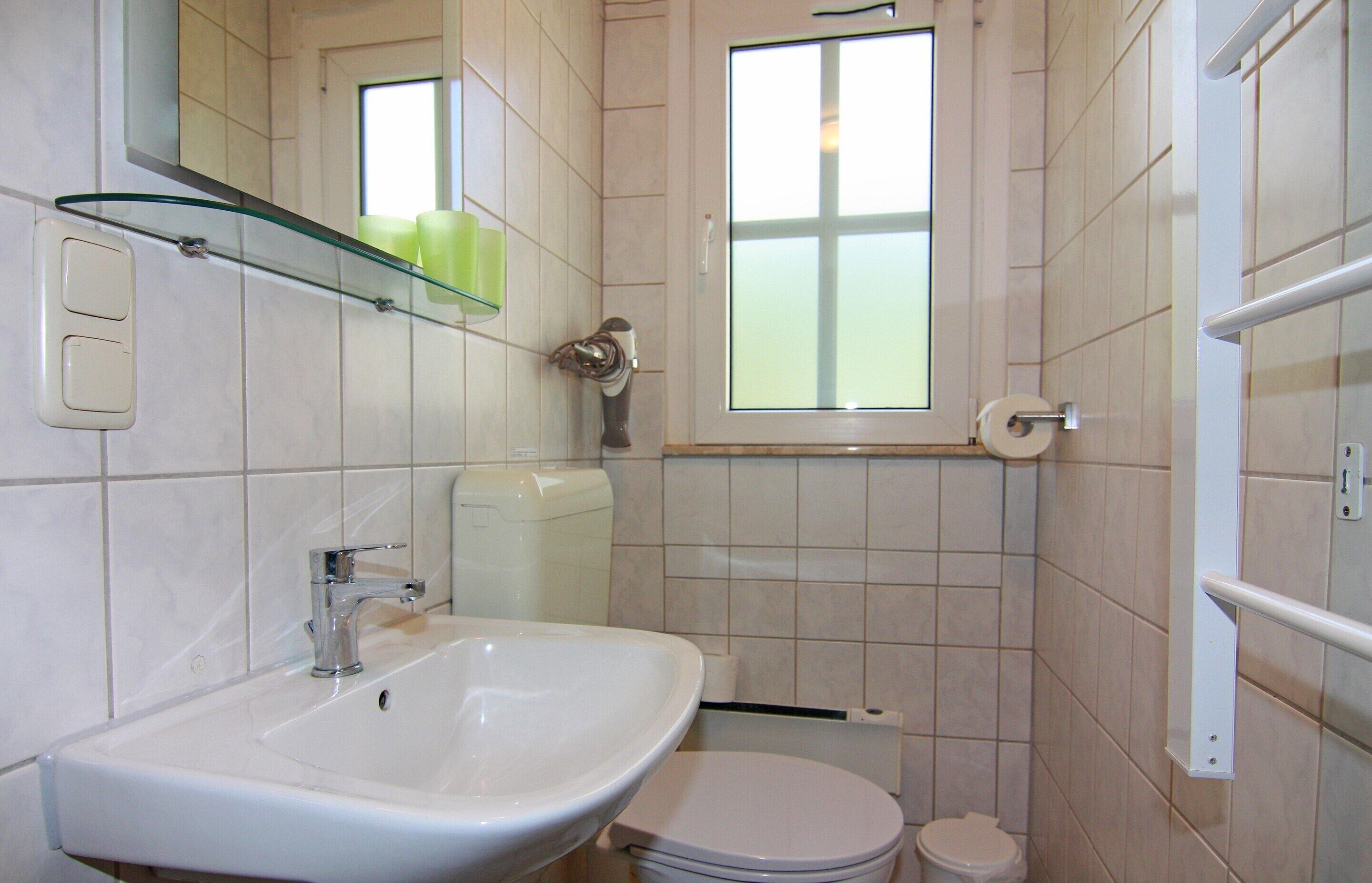 A bathroom with a white sink, toilet, and a glass shelf above the sink.