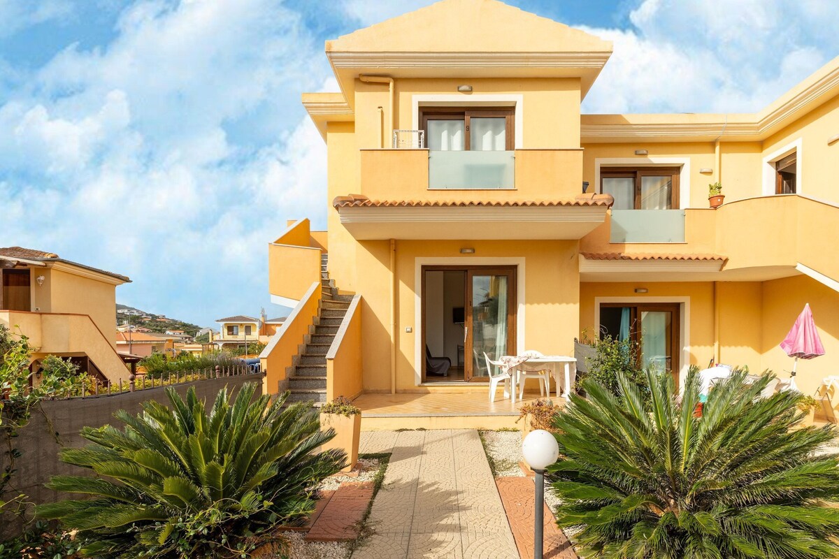 Ein zweistöckiges gelbes Gebäude mit Balkon, Treppe und Terrassenbereich mit Gartenmöbeln.