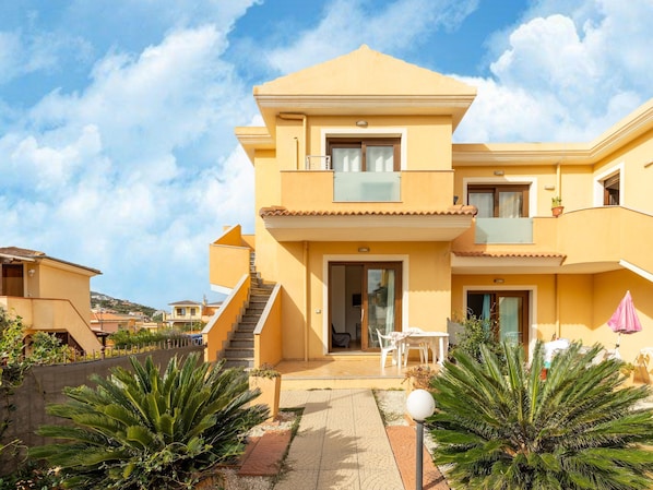 A two-story yellow building with a balcony, a staircase, and a patio area with outdoor furniture. - In the Residence, Terrace and air Conditioning (Castelsardo)