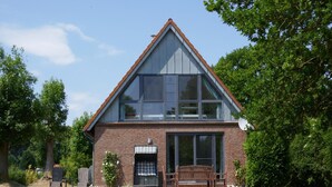 A two-story brick house with large windows, a front porch with a bench, and a satellite dish. - Ferienhaus Sturmfrei auf Fehmarn (Fehmarn)