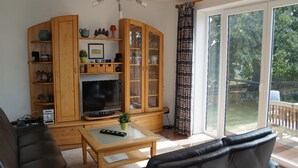 A living room with a TV, wooden cabinet, and a sliding glass door to the outdoors. - Ferienhaus Sturmfrei auf Fehmarn (Fehmarn)