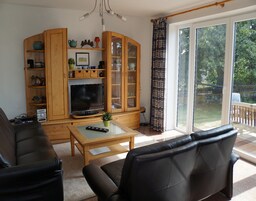 A living room with a TV, wooden cabinet, and a sliding glass door to the outdoors.
