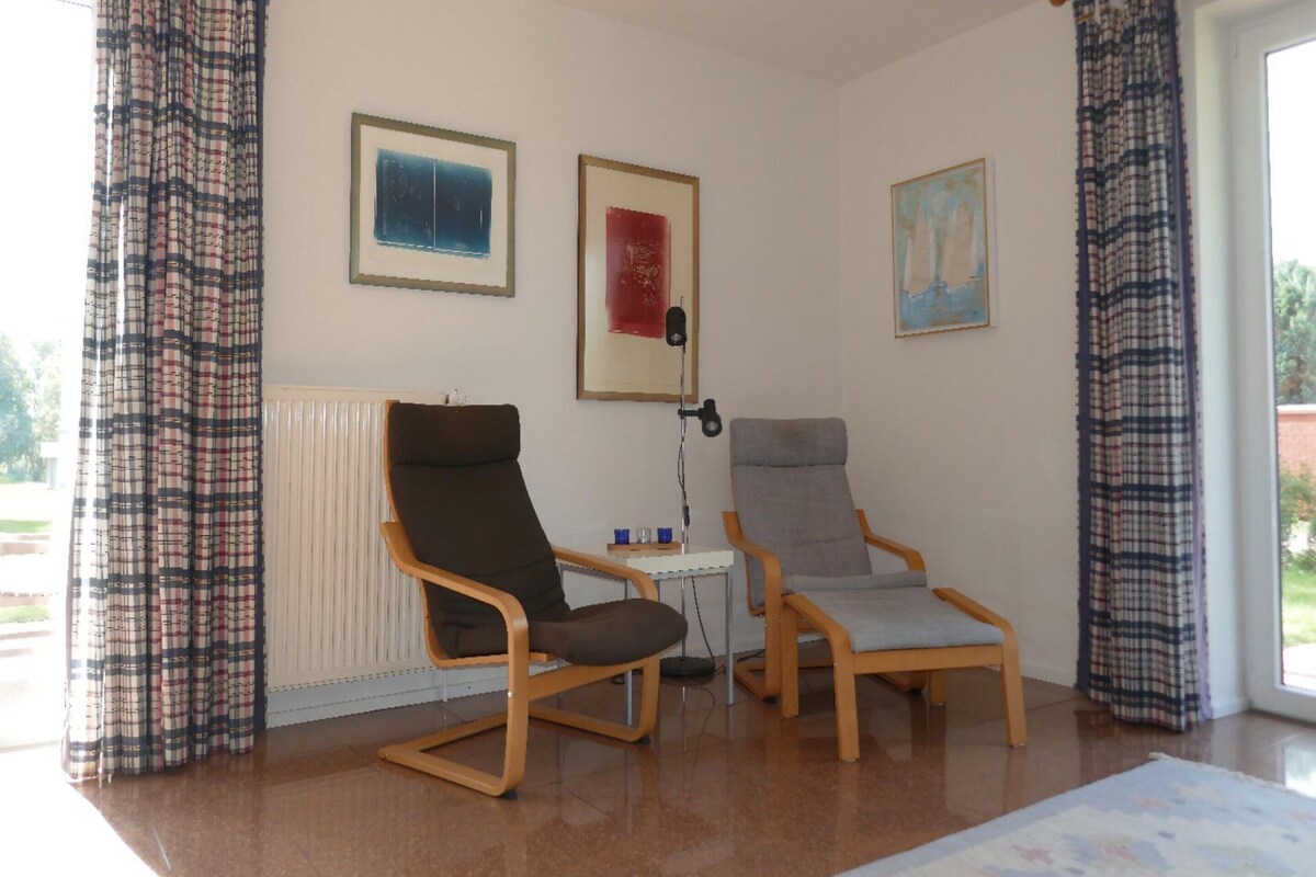 A room with two armchairs, a table, and three framed artworks on the wall.