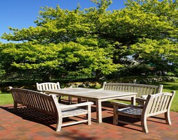 A patio area with a table and four chairs, surrounded by lush green trees.