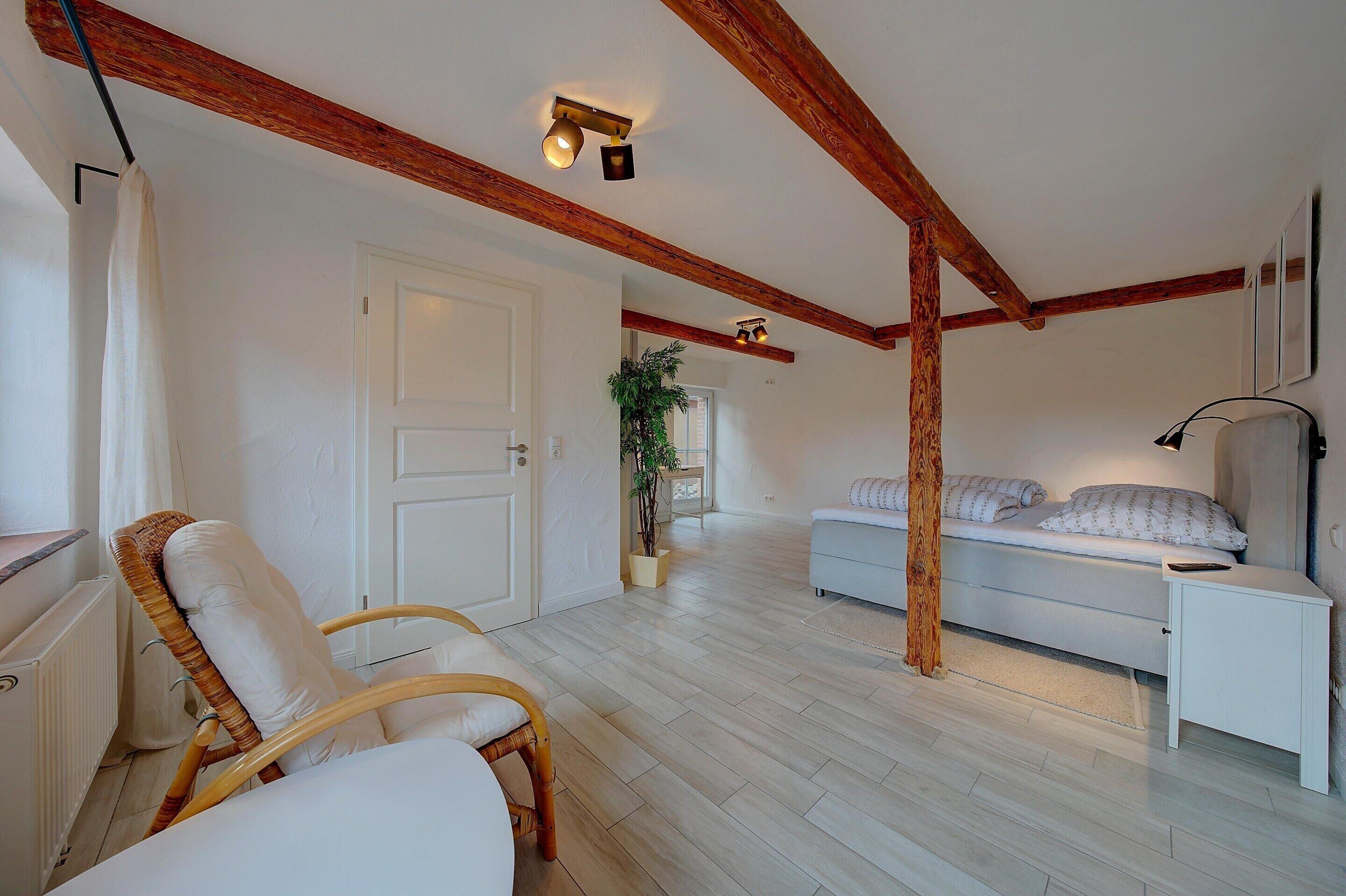 A room with a bed, a chair, a bedside table, and a plant.