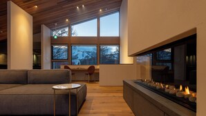 A modern interior with a sofa, a round table, a fireplace with candles, and large windows. - Shion (Kutchan)