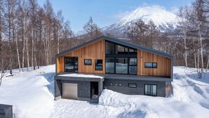 A modern two-story house with large windows, a garage, and a snowy landscape with a mountain in the background. - Shion (Kutchan)