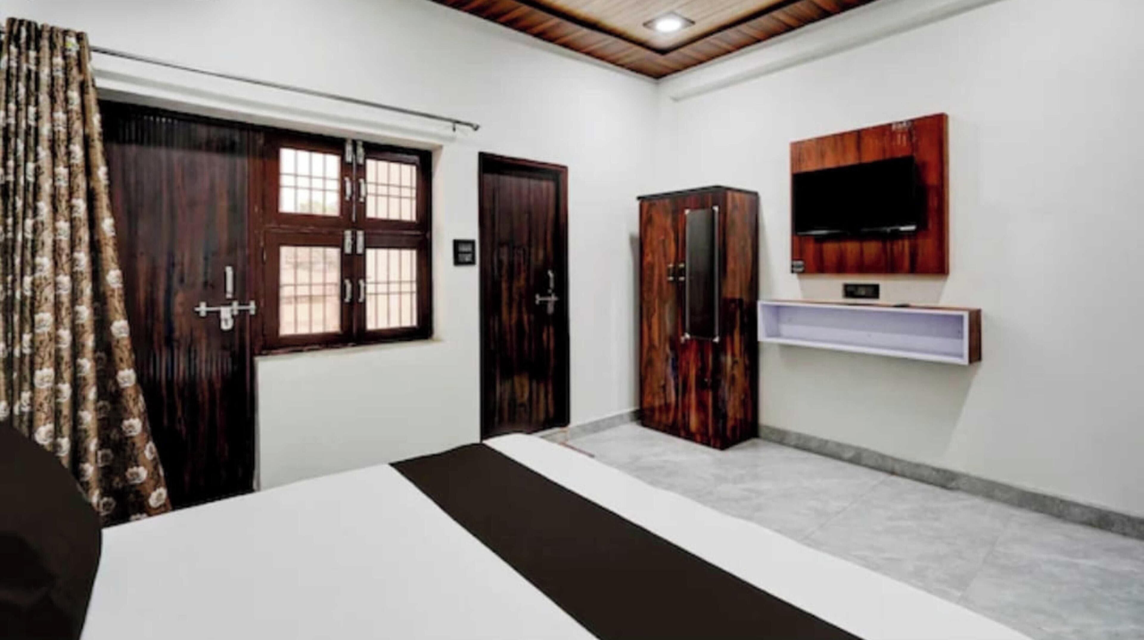 Une chambre à coucher avec un lit, deux portes, une armoire, un téléviseur fixé au mur et une fenêtre avec des rideaux.