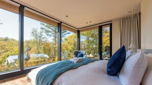 Een slaapkamer met een groot bed, uitzicht op bomen en een raam.