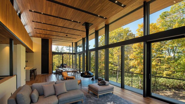 Een modern interieur met een ruime eethoek, een bank en uitzicht op bomen door grote ramen.