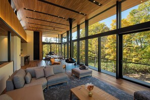 A modern interior with a large dining area, a sofa, and a view of trees through large windows. - Sena (Niseko)