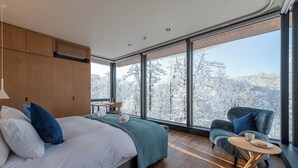 Een moderne slaapkamer met een groot raam, een bed, een zithoek en een klein tafeltje.