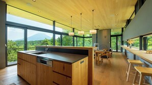 A modern kitchen with a wooden island, large windows, and a dining area with bar stools. - Hiyoku (Niseko)
