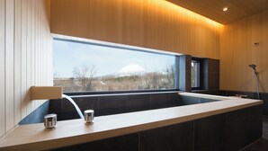A modern bathroom with a large bathtub, a window with a view of a mountain, and a shower area. - Hiyoku (Niseko)