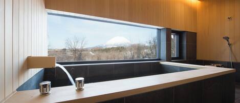 A modern bathroom with a large bathtub, a window with a view of a mountain, and a shower area.