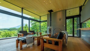 A spacious room with a large window offering a view of the outdoors, a fireplace, and wooden furniture. - Hiyoku (Niseko)