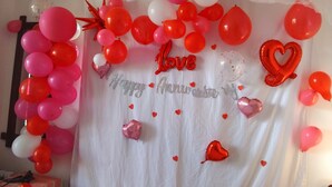 A room with a white curtain backdrop, red and pink balloons, and a 'Happy Anniversary' banner. - Ella Hillcrest Heaven (Ella)