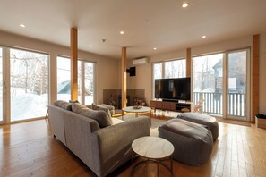 A spacious living room with a large sofa, ottomans, a coffee table, and a flat-screen TV. - Yukimine (Kutchan)