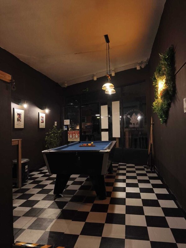 A billiards table in a room with a checkered floor, framed pictures on the walls, and a hanging light fixture.