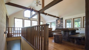 Un loft espacioso con escalera de madera, chimenea de piedra y ventanas amplias.