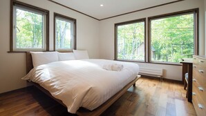 Un dormitorio con una cama grande, dos ventanas, un aparador y un radiador.