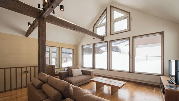 Un salón amplio con techo de madera, ventanas grandes, un sofá y una televisión.