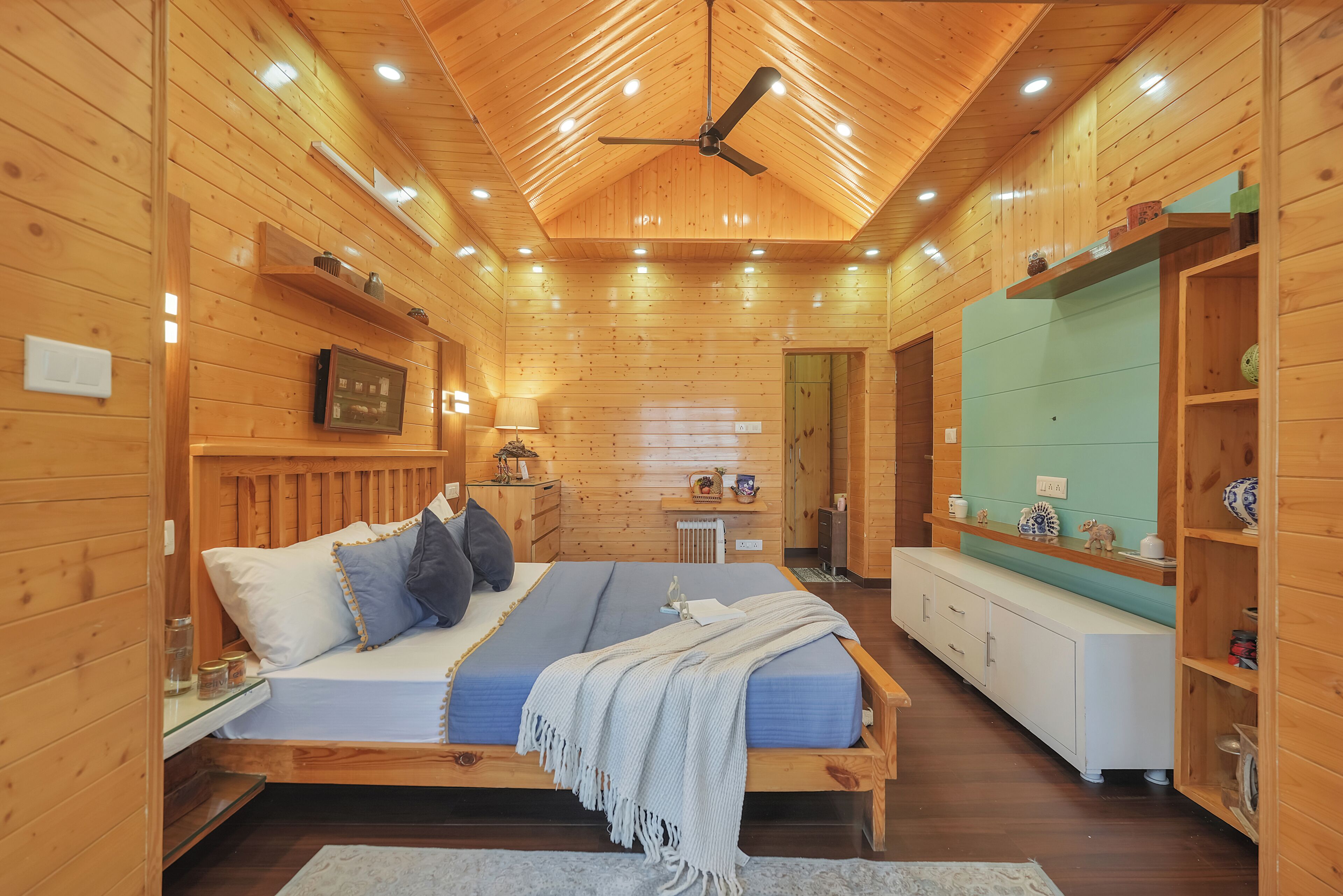 A wooden cabin interior with a bed, a white cabinet, and a ceiling fan.