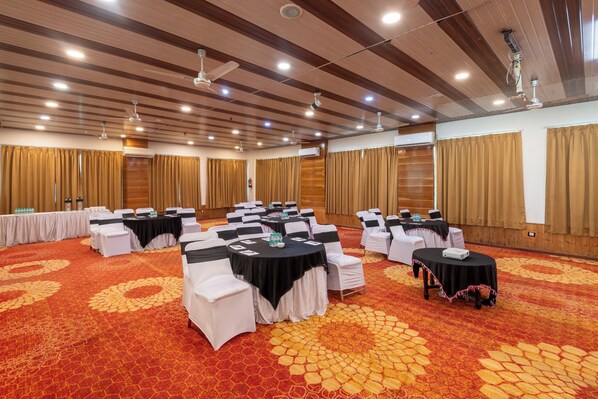 Un salón de conferencias con mesas redondas, sillas blancas y una alfombra estampada.
