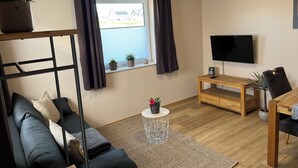 A modern living room with a sofa, a coffee table, a TV, and a window with curtains.