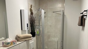 A modern bathroom with a glass-enclosed shower, a white sink with a wooden cabinet, a toilet, and a towel rack.