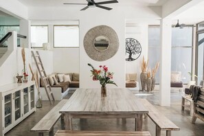 Uma sala ampla com uma mesa de jantar de madeira, uma escada e uma grande obra de arte na parede.