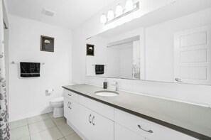 A modern bathroom with a white sink, vanity, and a large mirror with lights. There are two framed pictures on the wall, a toilet, and a shower curtain. - 5 Bedroom Estate | Sleeps17 | 65"TV | Free Parking (Kitchener)