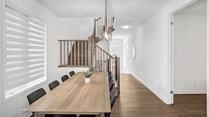 Un espace de salle à manger moderne avec une table en bois, des chaises noires, une plante en pot et un escalier avec des rampes en bois.