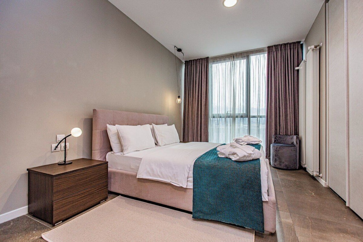 Une chambre d’hôtel moderne, équipée d’un lit, d’une table de chevet et offrant une vue sur l’extérieur.