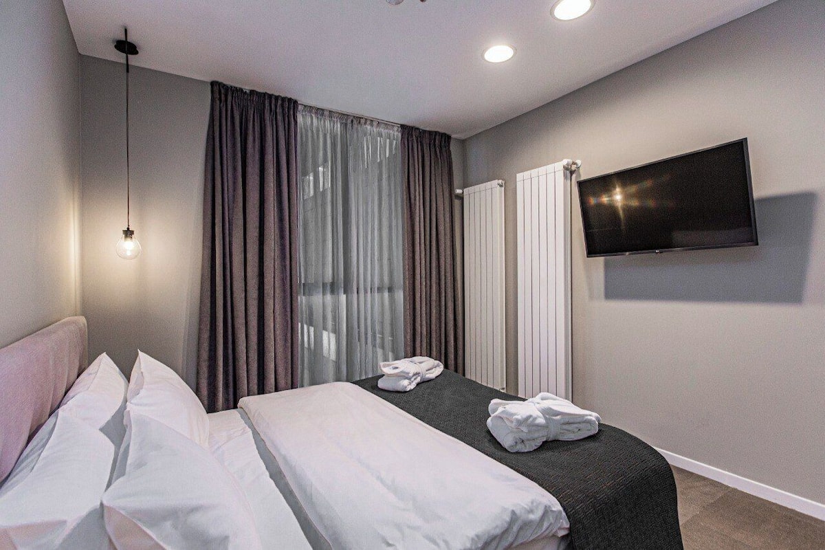 Une chambre d’hôtel avec un lit, une télévision, une fenêtre avec des rideaux et un radiateur.