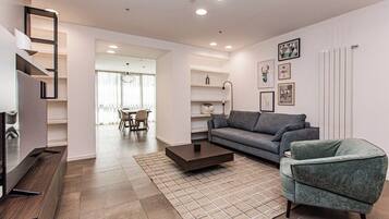 Ein modernes Wohnzimmer mit Sofa, Couchtisch und Sesseln, einer Treppe und einem Essbereich im Hintergrund.