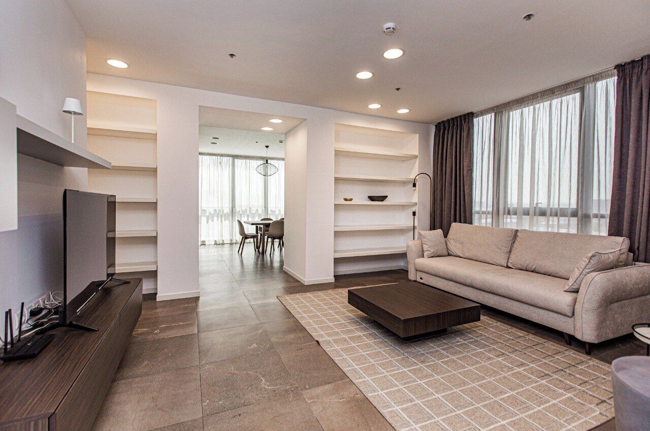 A modern living room with a sofa, coffee table, TV, and a dining area with chairs and a table.
