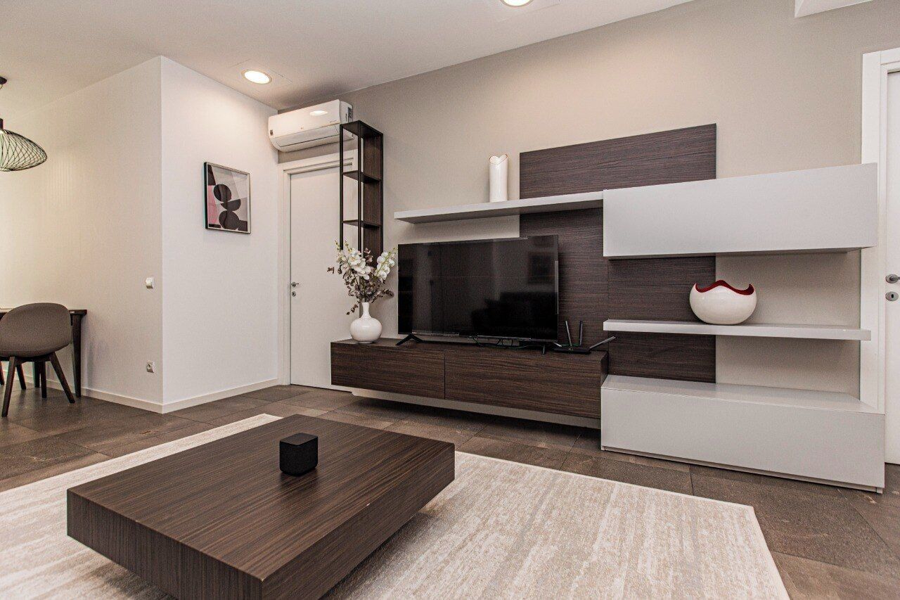 A modern living room with a flat-screen TV, dark wood furniture, and a white accent wall.