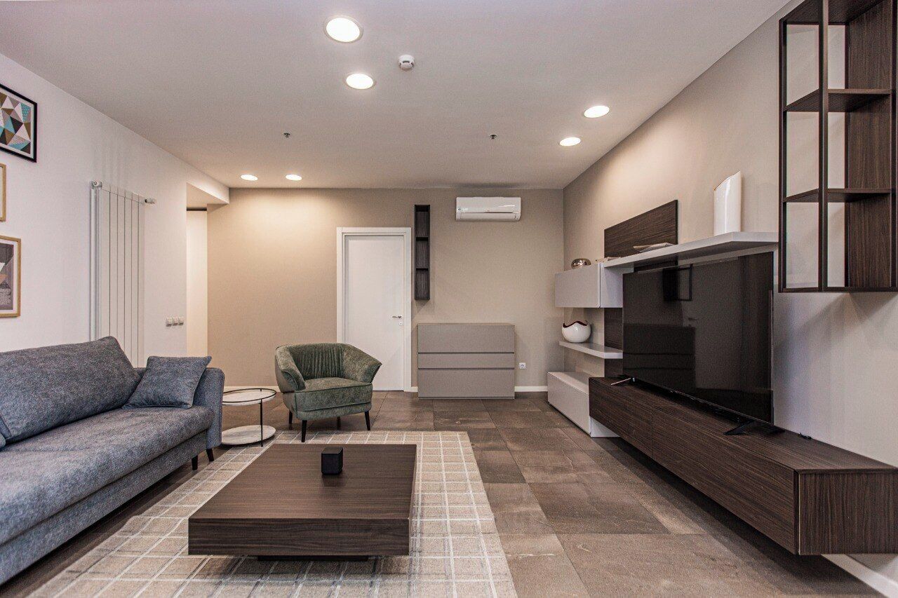 A modern living room with a sofa, armchair, coffee table, TV, and built-in shelving.