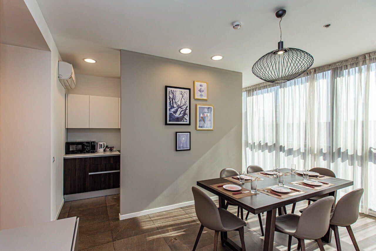A dining area with a table set for six, a kitchen with modern appliances, and a large window with sheer curtains.