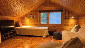 Ein gemütliches Schlafzimmer im Dachgeschoss mit Bett, Sofa, Fernseher und einem Fenster mit Blick auf Bäume.