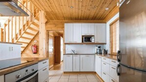Eine moderne Küche mit Holzbalken, weißen Schränken, Edelstahlgeräten und einem sichtbaren Feuerlöscher.