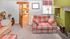 A cozy living room with a plaid sofa, a wooden door leading to a kitchen, and a green accent wall. - 1 bedroom accommodation in Bowness-on-Windermere (Bowness-on-Windermere)