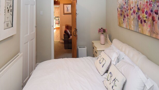 A bedroom with a bed, pillows, a nightstand, a painting, and a clock on the wall. - 1 bedroom accommodation in Bowness-on-Windermere (Bowness-on-Windermere)