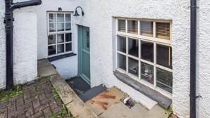A narrow alleyway with a white textured wall, a green door, and a window with blinds. - 1 bedroom accommodation in Bowness-on-Windermere (Bowness-on-Windermere)