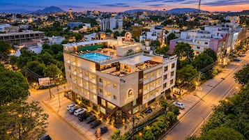 A multi-story hotel with a rooftop pool, surrounded by a cityscape at dusk.
