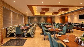 A restaurant with multiple dining tables and chairs, a bar area, and a seating section with patterned cushions.
